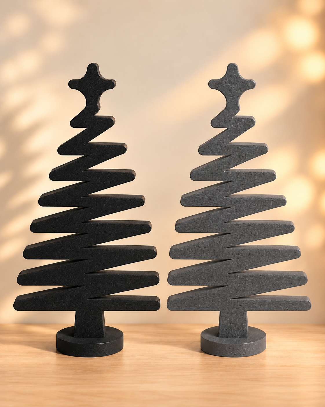 Zwei minimalistische Deko Weihnachtsbäume aus PE Schaumstoff in Schwarz und Dunkelgrau mit Stern und rundem Standfuß auf einer hellen Holzfläche.