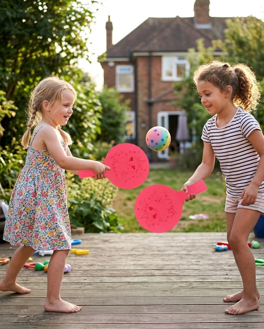 Zwei Kinder spielen draußen im Garten mit roten Schlägern und einem kleinen Ball